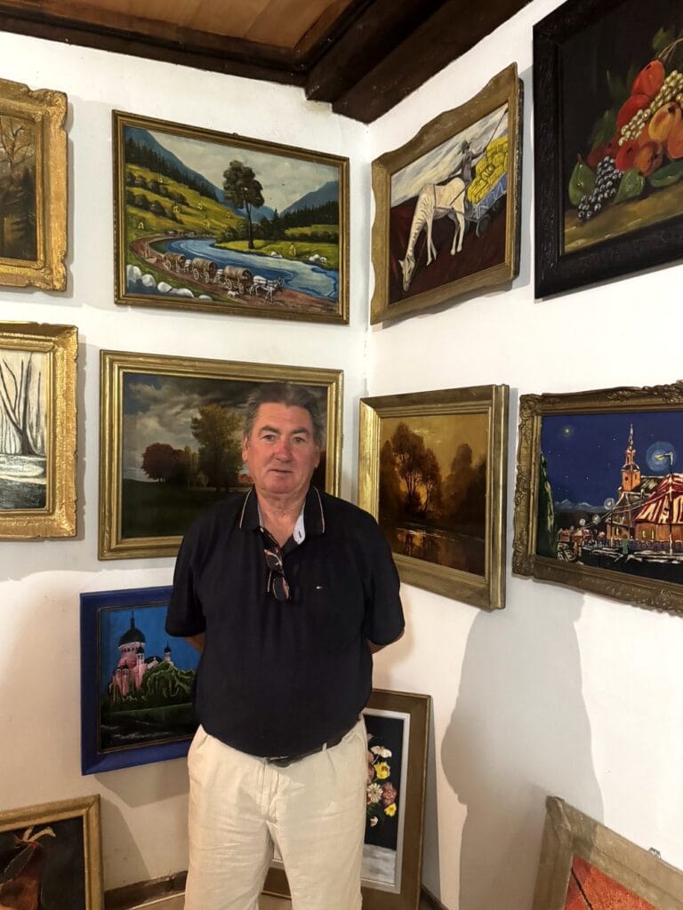 Pictorul Luis Ludovic Garcia Camarero în fața unui perete acoperit de picturi înrămate, în galeria din Frata